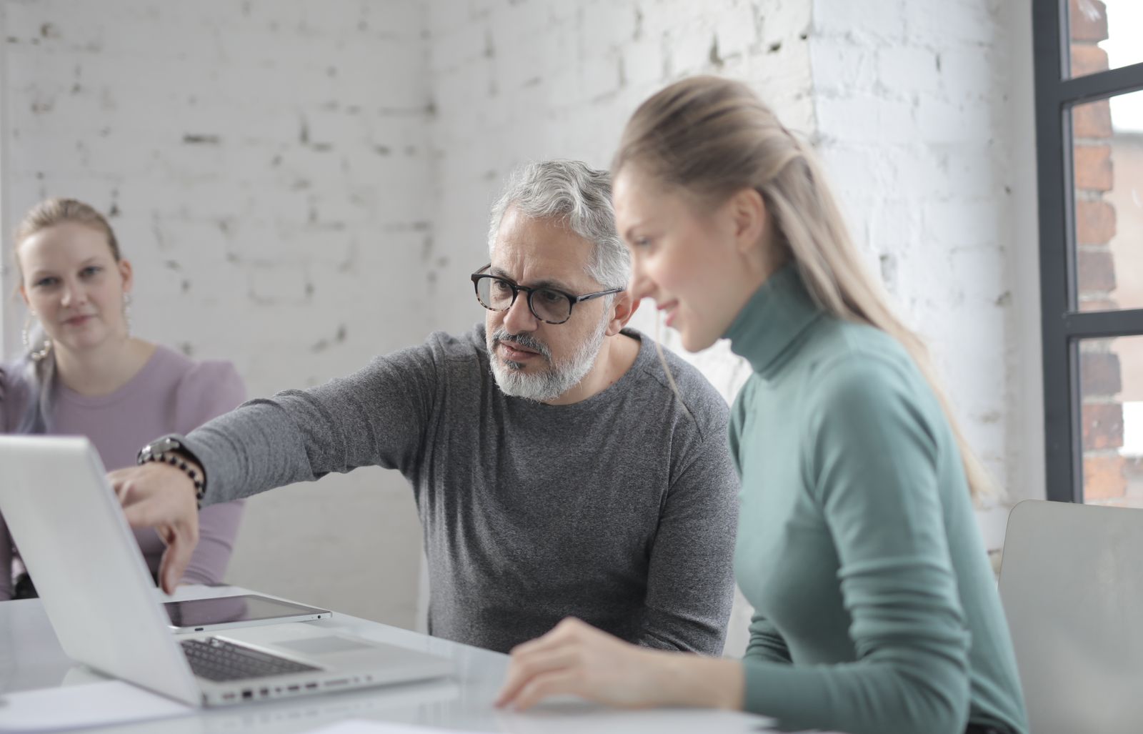 An experienced colleague coaching another at a laptop.